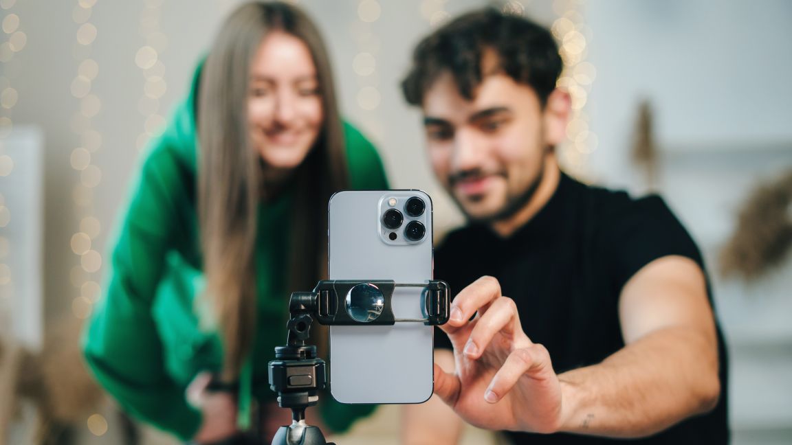 zwei junge Menschen, die ein Smartphone auf einem Stativ bedienen